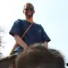 man with mud on face enjoying riding an elephant