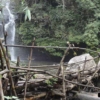woman trekking over small bamboo bridge by waterfall