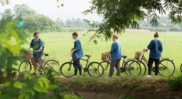 men and women walking their bicycles along rice paddy