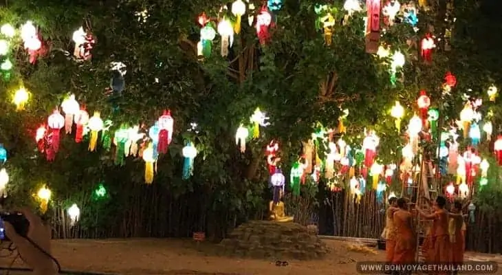 monks under tree decorated with traditional thai lanterns during yeepeng festival